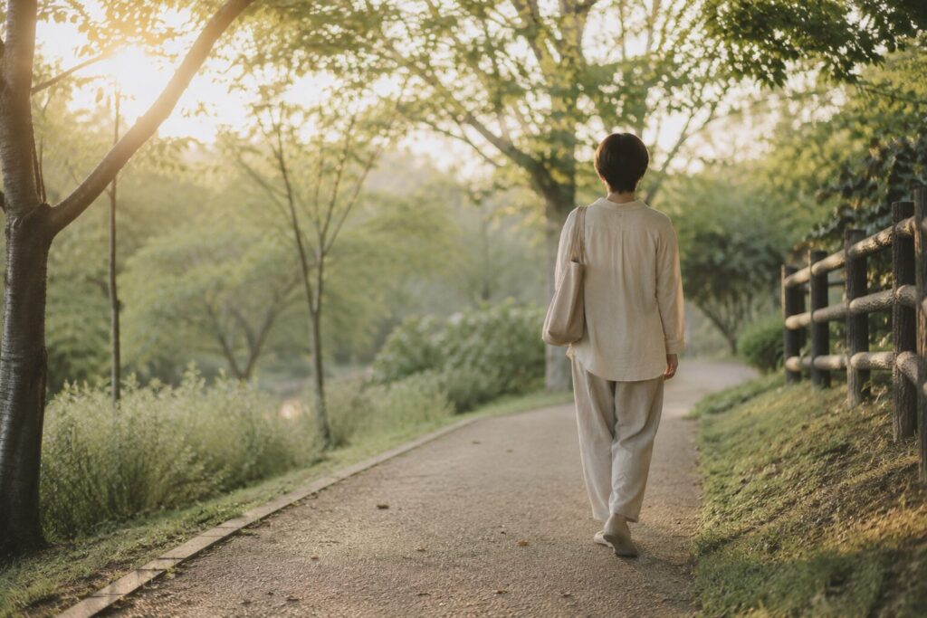 40代女性、公園の遊歩道を朝日を浴びながらゆっくり歩く後ろ姿