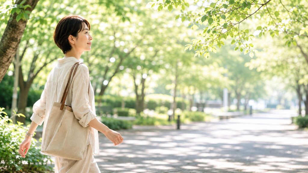40代日本人女性、公園の木陰を歩く横顔、朝の日差しが木漏れ日になって差し込む、帽子なし